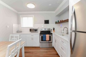 Una cocina moderna con armarios blancos, un refrigerador de acero inoxidable, un microondas, un horno y un lavabo.