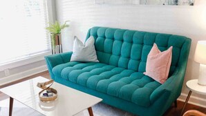 Ein smaragdgrünes Sofa mit zwei Kissen, ein kleiner weißer Tisch mit Tablett und eine Lampe auf einem Beistelltisch.