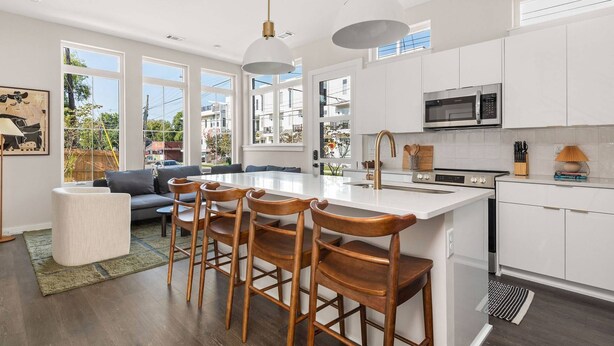 Una cocina moderna con armarios blancos, una isla central con taburetes, un microondas y una estufa.