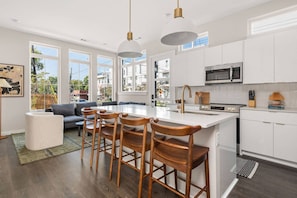 A modern kitchen with white cabinetry, a central island with bar stools, a microwave, and a stove.