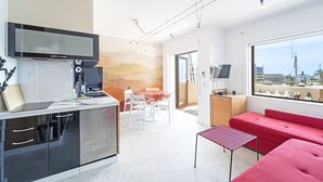 Een moderne keuken met een televisie, een eethoek met tafel en stoelen, een rode bank en een groot raam met uitzicht over de stad.