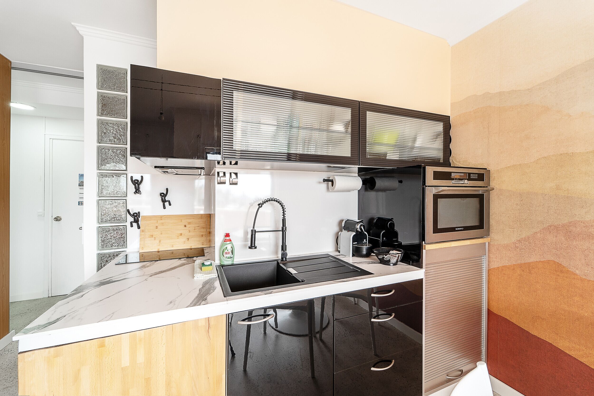 A modern kitchen with a black and white marble countertop, a built-in sink, a stainless steel range hood, and a microwave.