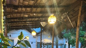 An outdoor seating area with wooden tables and chairs, hanging lights, and potted plants. - Cactus Arugambay (Arugam Bay)