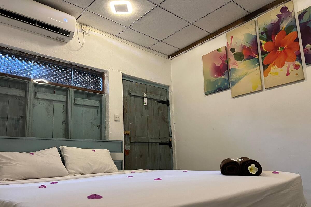 Una habitación de hotel con una cama, un ventanal con vistas y una pared con tres cuadros.