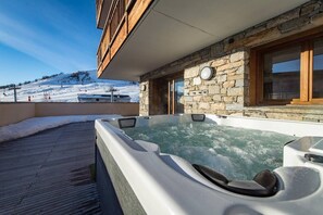 A spa area with a hot tub and stone walls, overlooking a snowy landscape. - 12-person flat with jacuzzi in a new residence at the foot of the slopes (LA TOUSSUIRE)