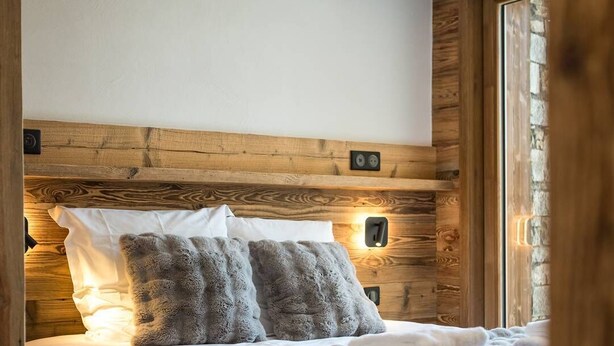 Una cama con cabecera de madera, dos almohadas, una colcha y una mesita de noche con una lámpara.