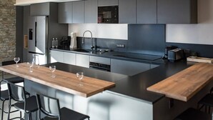 Una cocina moderna con una isla central, muebles negros y grises y una pared decorativa de piedra.