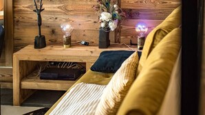 Ein gemütliches Wohnzimmer mit Holzwand, einem flachbildfernseher über einem Couchtisch aus Holz und einem bequemen, gelben Sofa mit Kissen.
