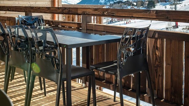 Eine Holzterrasse mit Tisch und Stühlen mit Blick auf eine verschneite Berglandschaft.