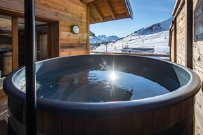 A wooden cabin with a hot tub and a view of a snowy mountain landscape.
