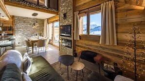A cozy cabin interior with a stone wall, wooden beams, a dining area, a fireplace, and a TV. - Duplex for 6/8 people in a new residence on the slopes (LA TOUSSUIRE)