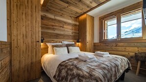 A cozy wooden cabin bedroom with a large bed, a window with a view of a snowy landscape, and a rustic wooden wall. - Apartment for 6/8 people with jacuzzi in a new residence on the slopes (LA TOUSSUIRE)
