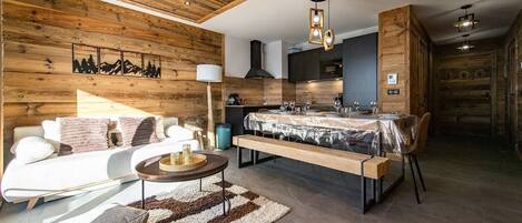 Una cocina moderna con detalles de madera, un comedor con bancos y una sala de estar con sofá y mesa de centro.