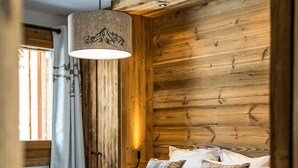 Een knus slaapkamer met een houten hoofdbord, een bed met witte lakens en geruite kussens, een hanglamp en een raam met gordijnen.