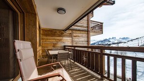 Een houten balkon met een tafel en stoelen, met uitzicht op een besneeerd berglandschap.