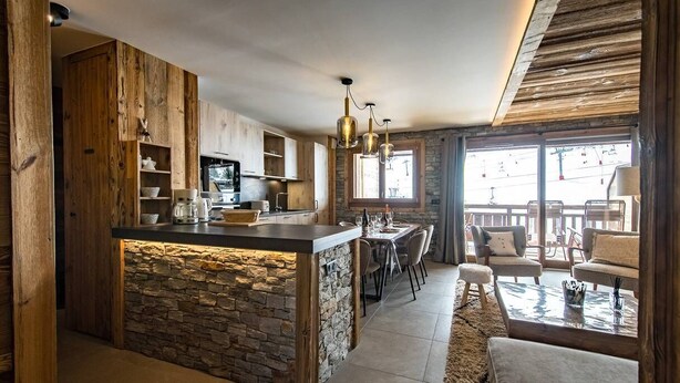Een moderne keuken met een stenen kookeiland, houten kastjes en een eethoek met een stenen vloer.