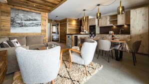 Een moderne keuken met houten kastjes, een eethoek met tafel en stoelen, en een woonkamer met een bank en fauteuils.