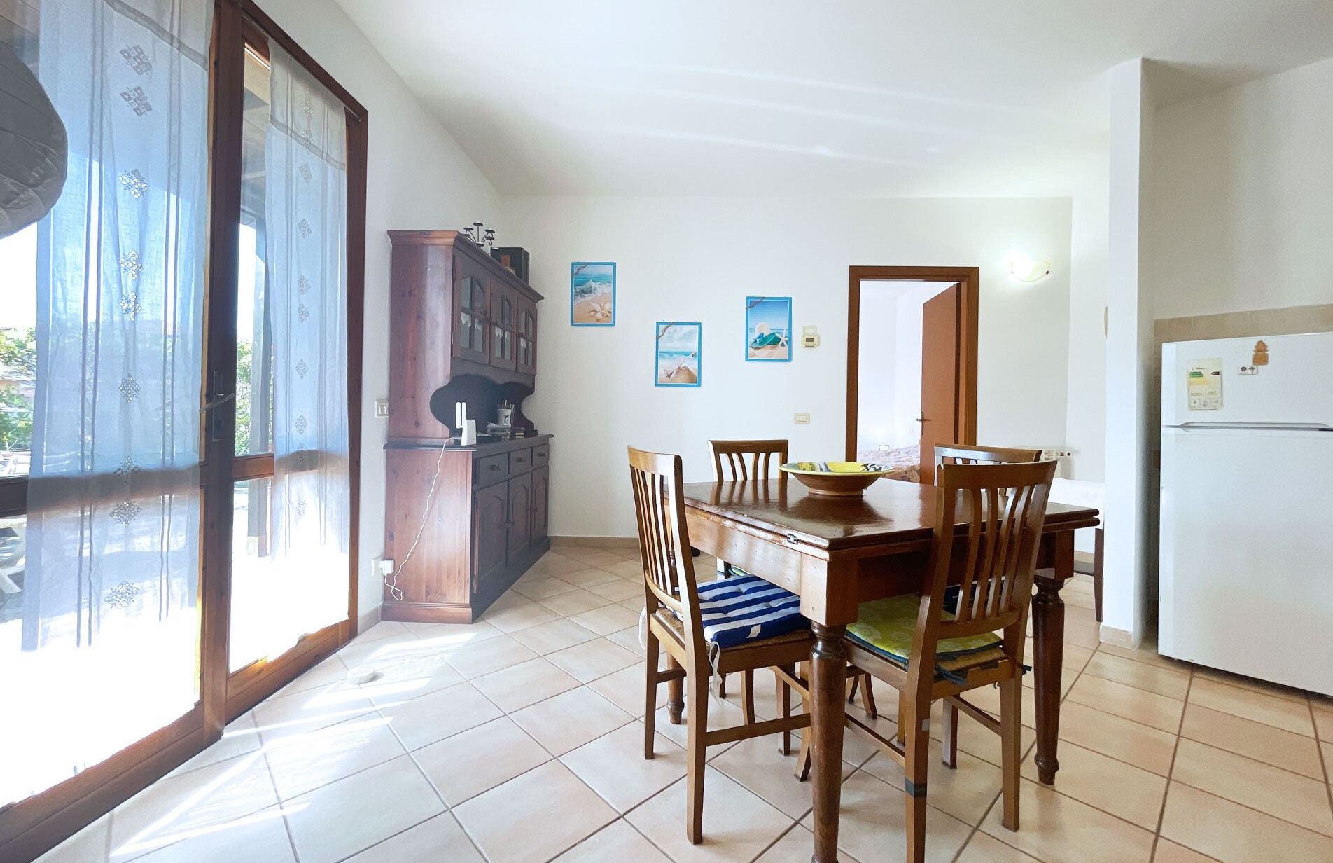 A dining area with a wooden table and chairs, a cabinet, and a refrigerator.