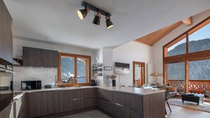 Une cuisine moderne dotée d’un grand îlot central, de meubles en bois et offrant une vue sur un paysage enneigé grâce à de grandes fenêtres.