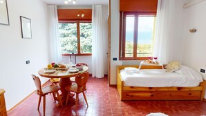Une pièce chaleureuse avec un lit en bois, une table à manger avec des chaises et une vue sur l’extérieur grâce à de grandes fenêtres.
