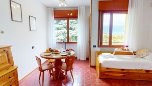 Une pièce avec un lit en bois, une table à manger avec des chaises et une fenêtre donnant sur des arbres.