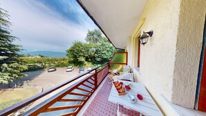 Un balcon avec une table dressée pour le petit-déjeuner, donnant sur un parking et offrant une vue panoramique sur les arbres et les montagnes.