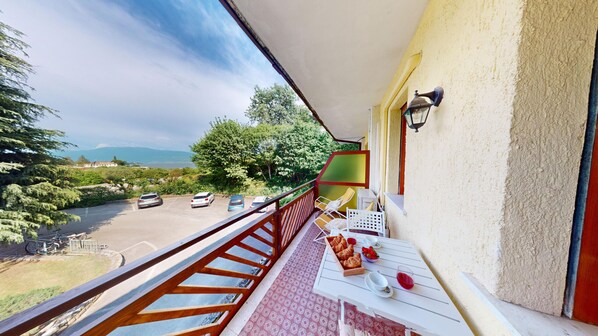 Un balcone con un tavolo apparecchiato per la colazione, affacciato su un'area di parcheggio e una vista panoramica di alberi e montagne.