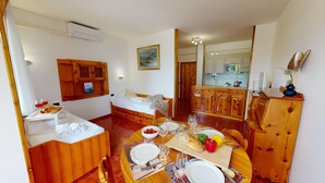 Une pièce compacte comprenant un lit, une table à manger pour deux personnes, un coin cuisine et une petite salle de bain.