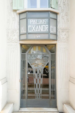 A building entrance with ornate architectural details and a sign reading "PALAISE EXANOR EIII".