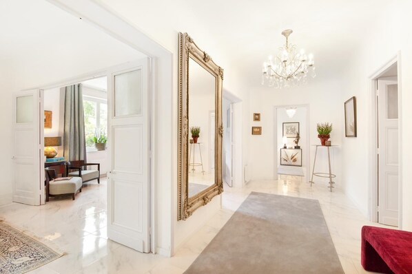 A spacious hallway with a large ornate mirror, a chandelier, and a red bench.