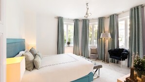 A modern bedroom with a large bed, a bedside table, a chair, and a floor lamp. - 3 Bedroom Apartment in Heart of Cannes (Cannes)