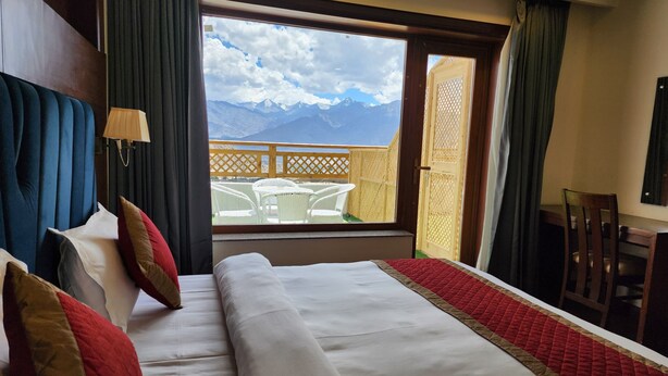 Camera d'hotel con un letto grande, vista sulle montagne e un balcone con mobili da esterno.