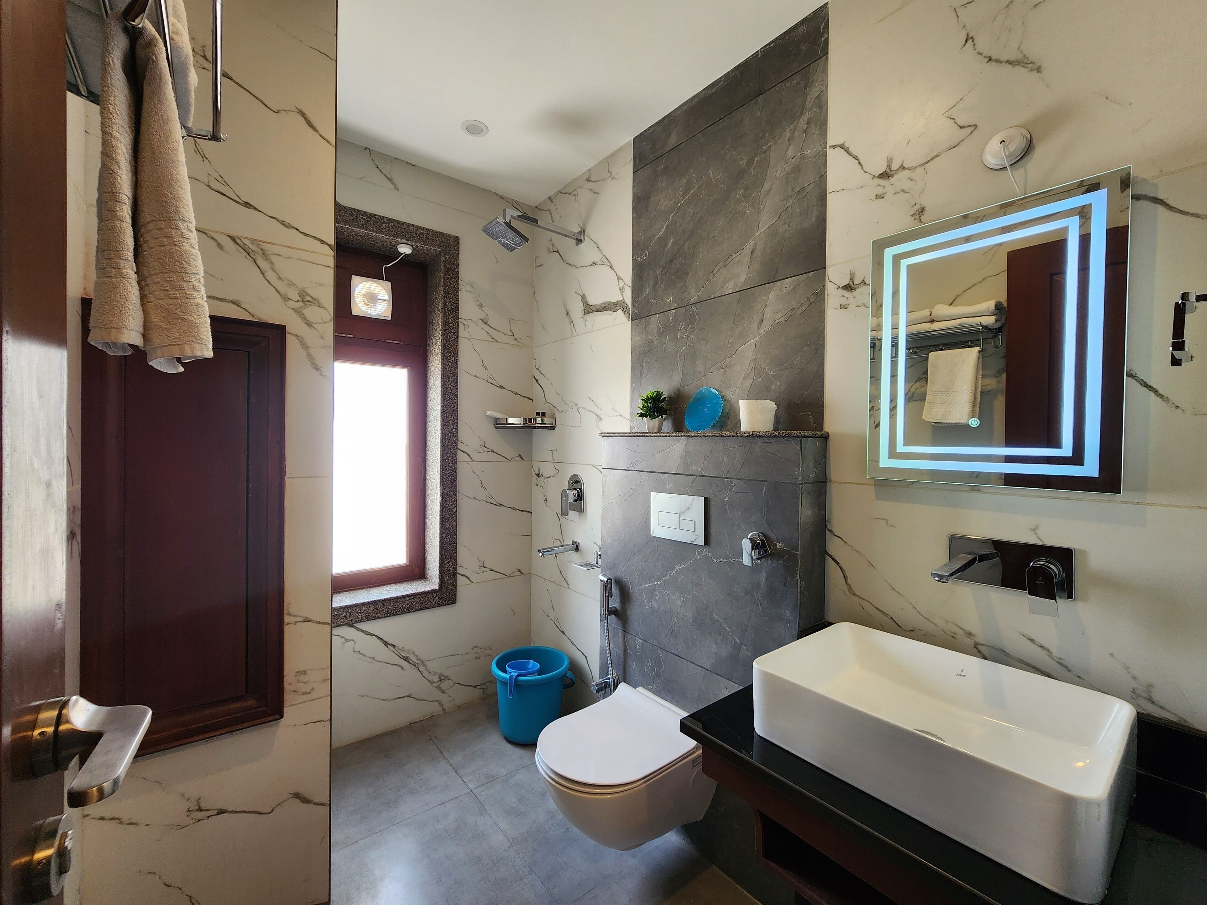 A modern bathroom with a marble wall, a large mirror, a bathtub, and a toilet.