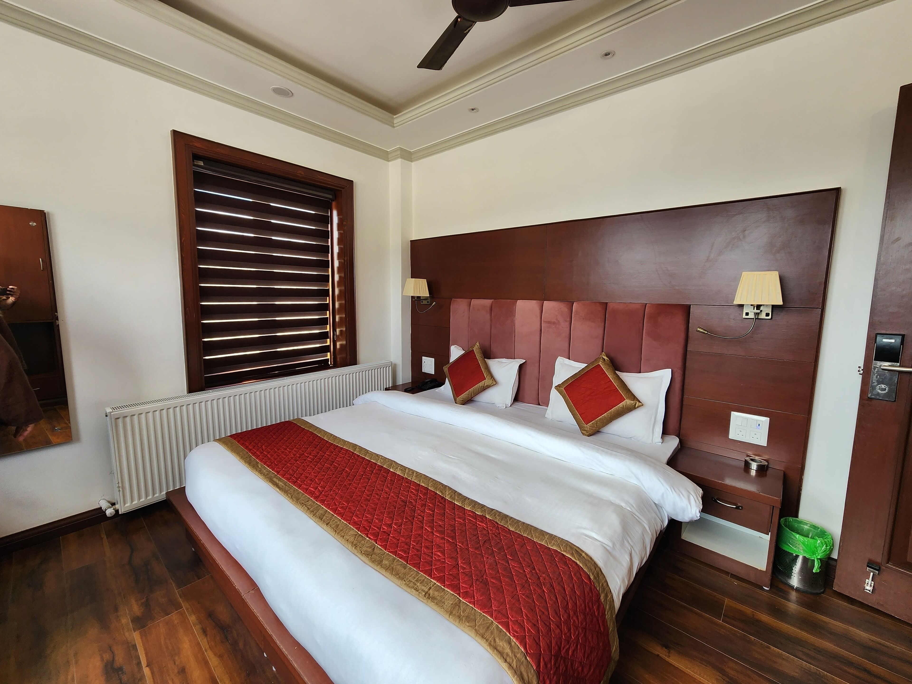 A hotel room with a large bed, wooden headboard, and a window with blinds.