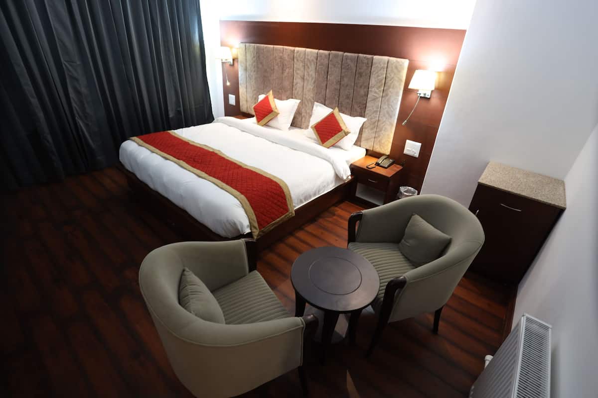 A hotel room with a large bed, two armchairs, a small round table, a nightstand, and a desk.