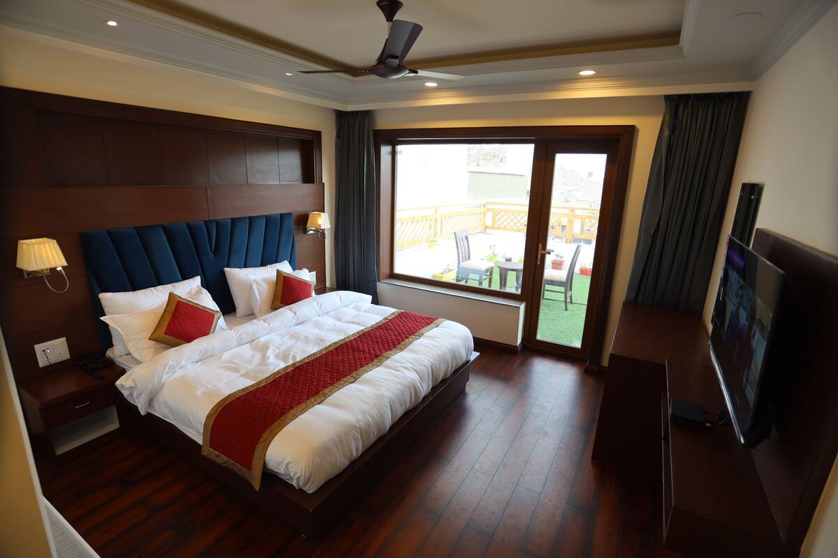 A hotel room with a large bed, a ceiling fan, a television, and a view of the outdoors.