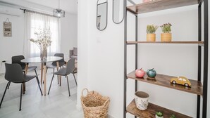 A modern living room with a round dining table, grey chairs, a woven basket, and a wooden shelf with decorative items.