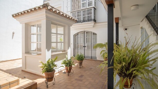 A spacious courtyard with a tiled floor, potted plants, a small covered seating area, and a gated entrance.