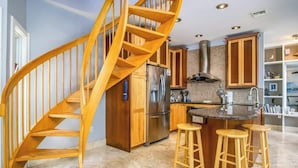 A kitchen with a wooden spiral staircase, stainless steel appliances, and wooden stools. - Serenity Retreat- 2/2 Townhouse, Dock & Pool (Key West)