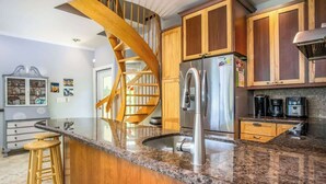 A kitchen with wooden cabinets, a stainless steel refrigerator, a granite countertop, and a wooden spiral staircase. - Serenity Retreat- 2/2 Townhouse, Dock & Pool (Key West)