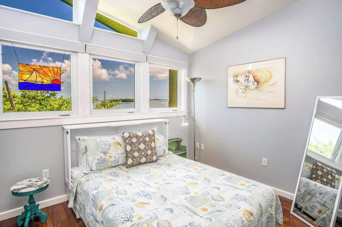 Una camera da letto con un letto, una finestra vista, una ventola a soffitto e un quadro appeso al muro.