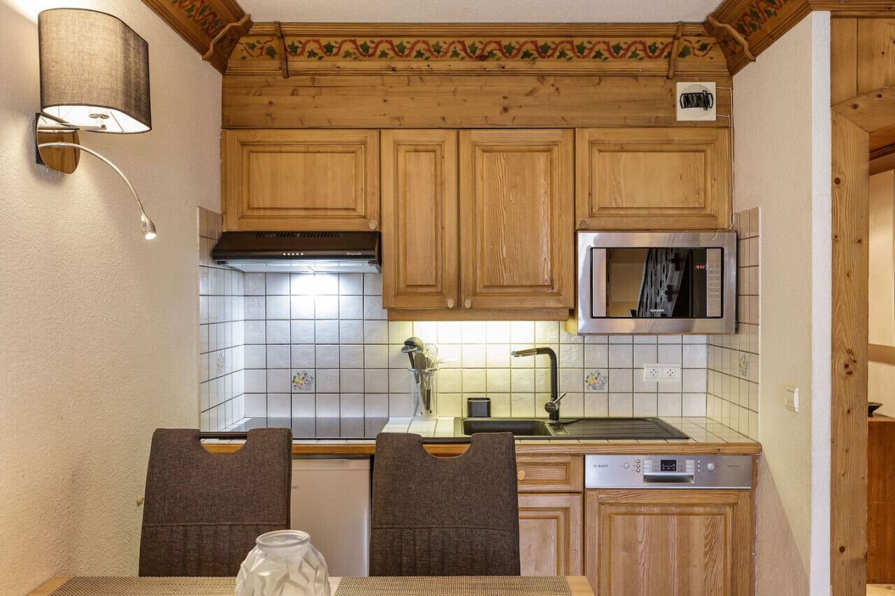 Cocina compacta con armarios de madera, un microondas, un fregadero y un lavavajillas.