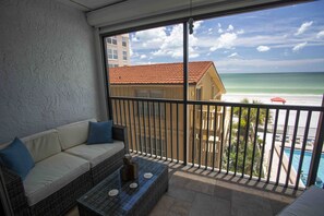 Un balcon avec vue sur la plage, une piscine et un bâtiment avec un toit rouge.