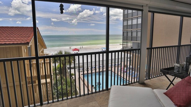 A balcony with a view of a beach, a pool, and a building with a red roof.