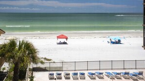 A beach with a row of sun loungers, a red and a blue umbrella, and a fenced area.