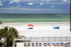 Une plage avec une rangée de chaises longues, un parasol rouge et un parasol bleu, et une zone délimitée par une clôture.