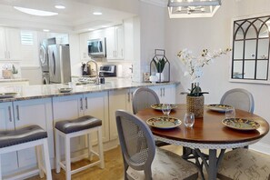 Une cuisine moderne avec des meubles blancs, des appareils en acier inoxydable et un coin repas comprenant une table et des chaises en bois.