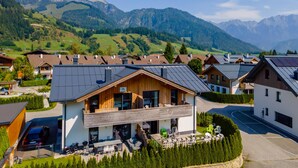 A modern building with a wooden facade, a balcony, and a view of a mountainous landscape. - Modern apartment with woodstove & large terrace (Leogang)