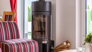 A modern living room with a large black wood-burning stove, a striped sofa, and a dining table with a glass. - Modern apartment with woodstove & large terrace (Leogang)