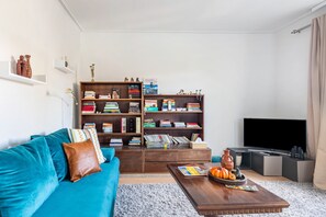 Un salon avec un canapé bleu, une bibliothèque en bois, une table basse avec des magazines et un téléviseur à écran plat.